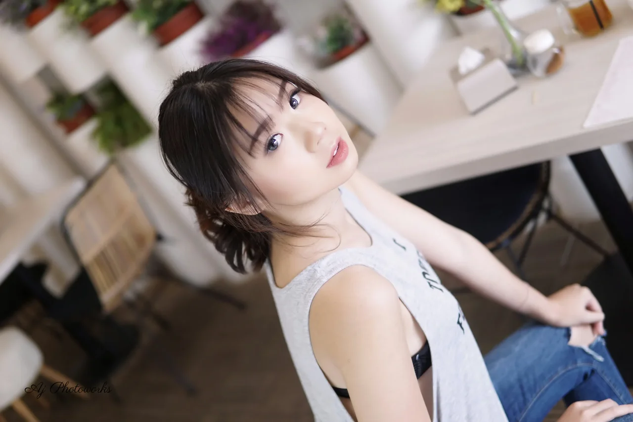 A young woman looks directly at the camera in a softly lit cafe setting.