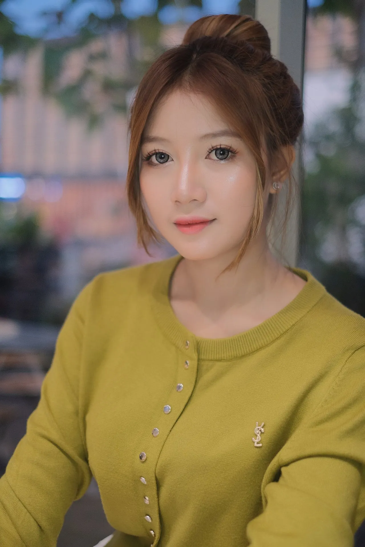 A woman with striking eyes looks softly toward the camera indoors, wearing a chartreuse cardigan.