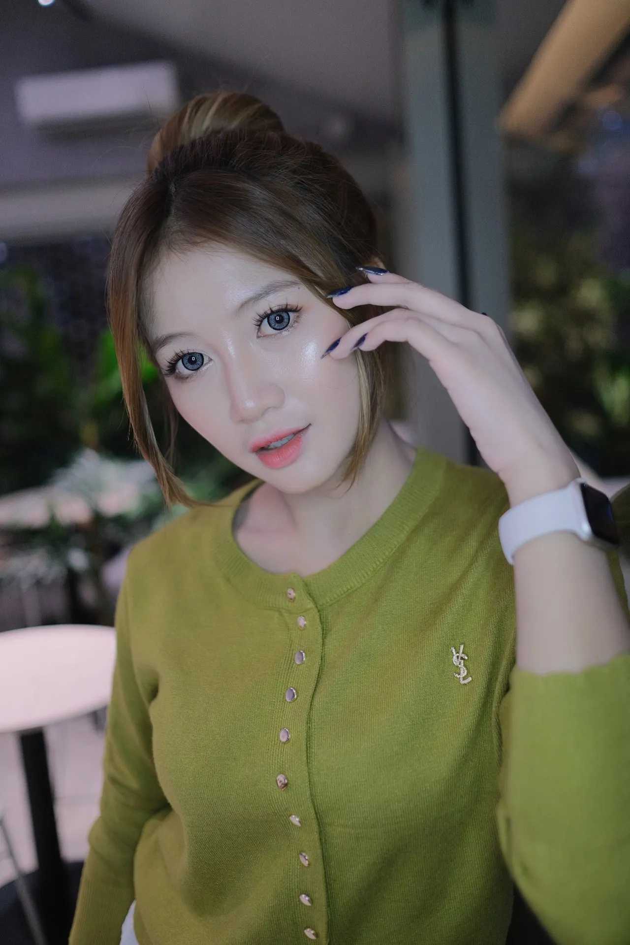 A woman in a green cardigan poses intimately in a dimly lit, soft-focus setting.